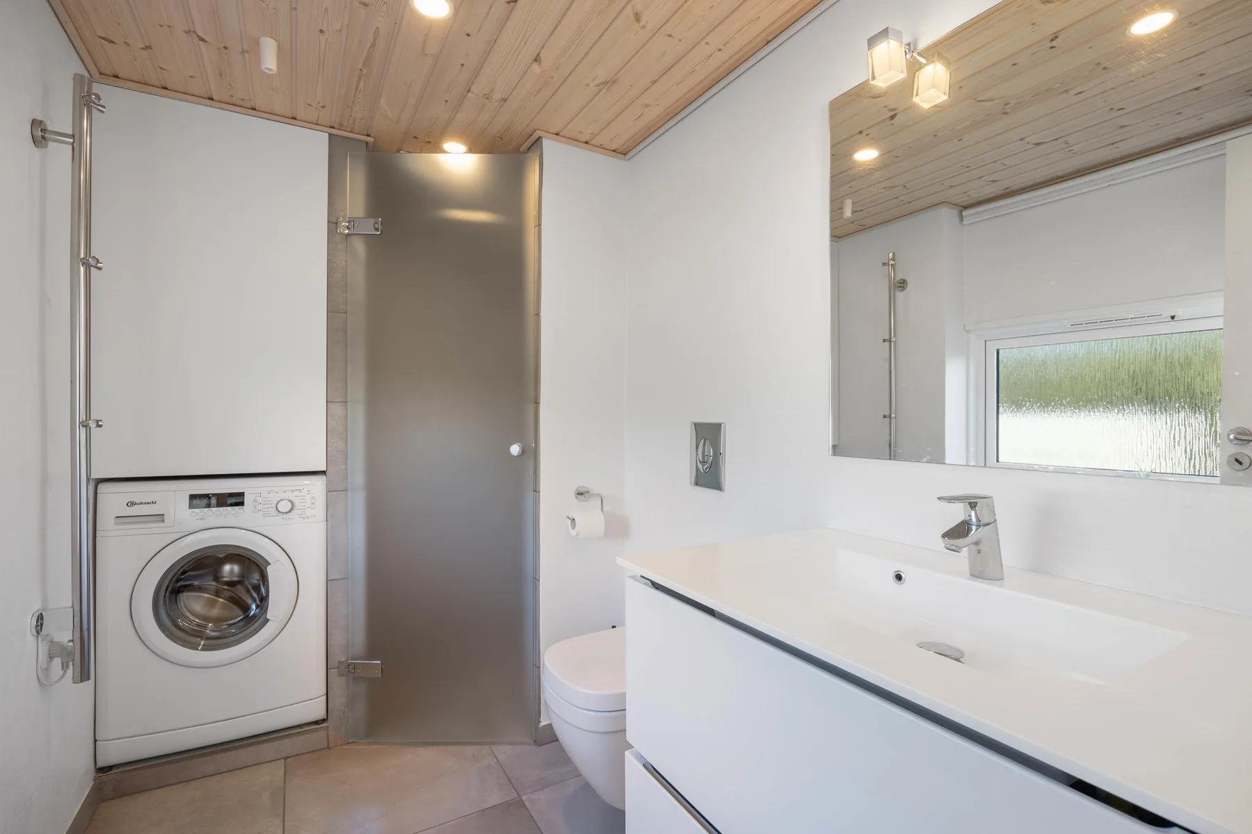 Un baño luminoso con lavabo, espejo y lavadora.