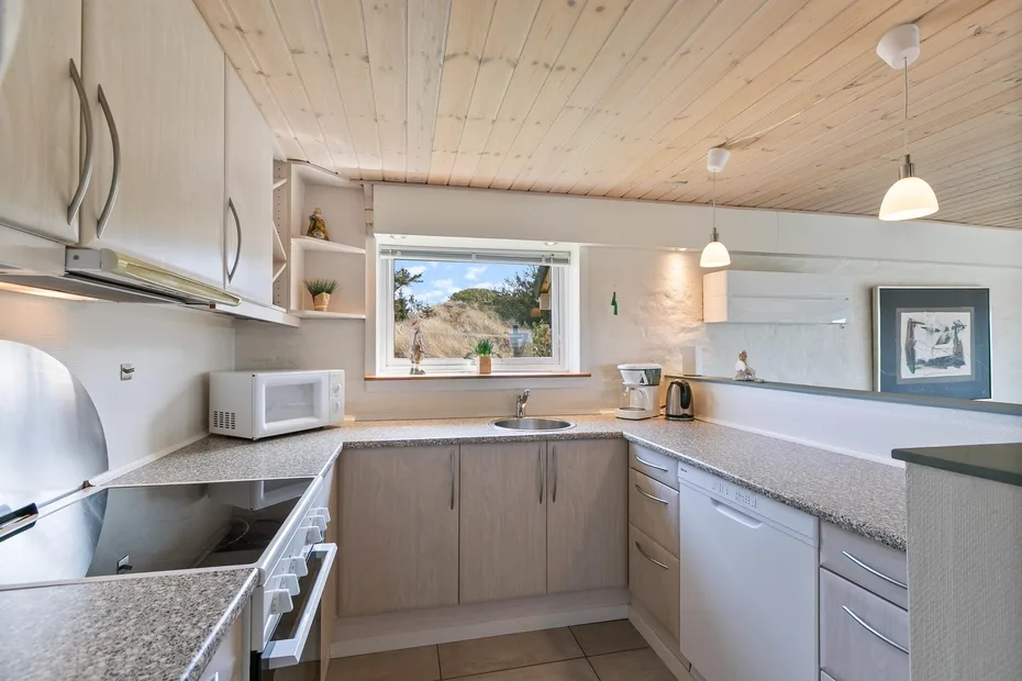 Una cocina luminosa con gabinetes claros, una encimera y una ventana sobre el fregadero.
