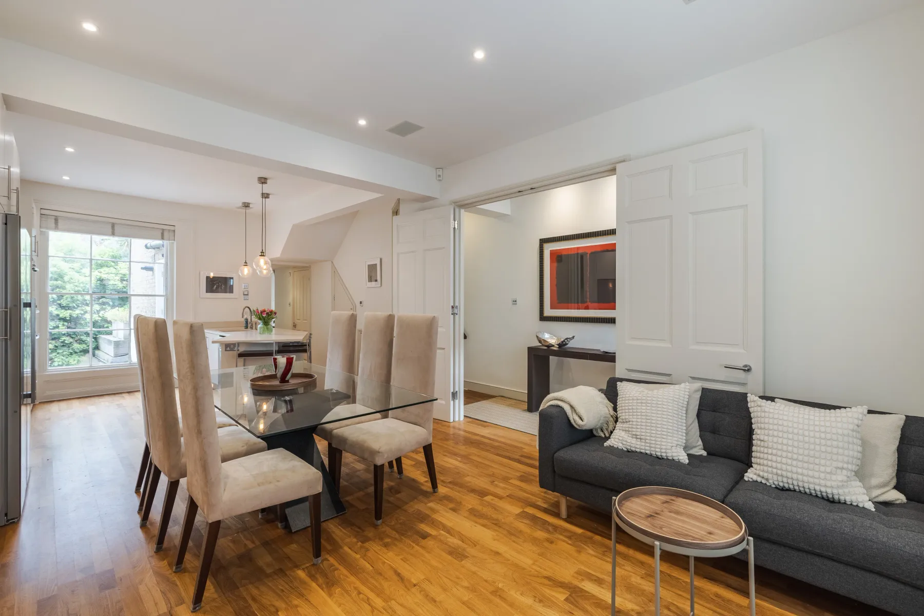 A bright living and dining area with a dark sofa and glass dining table.