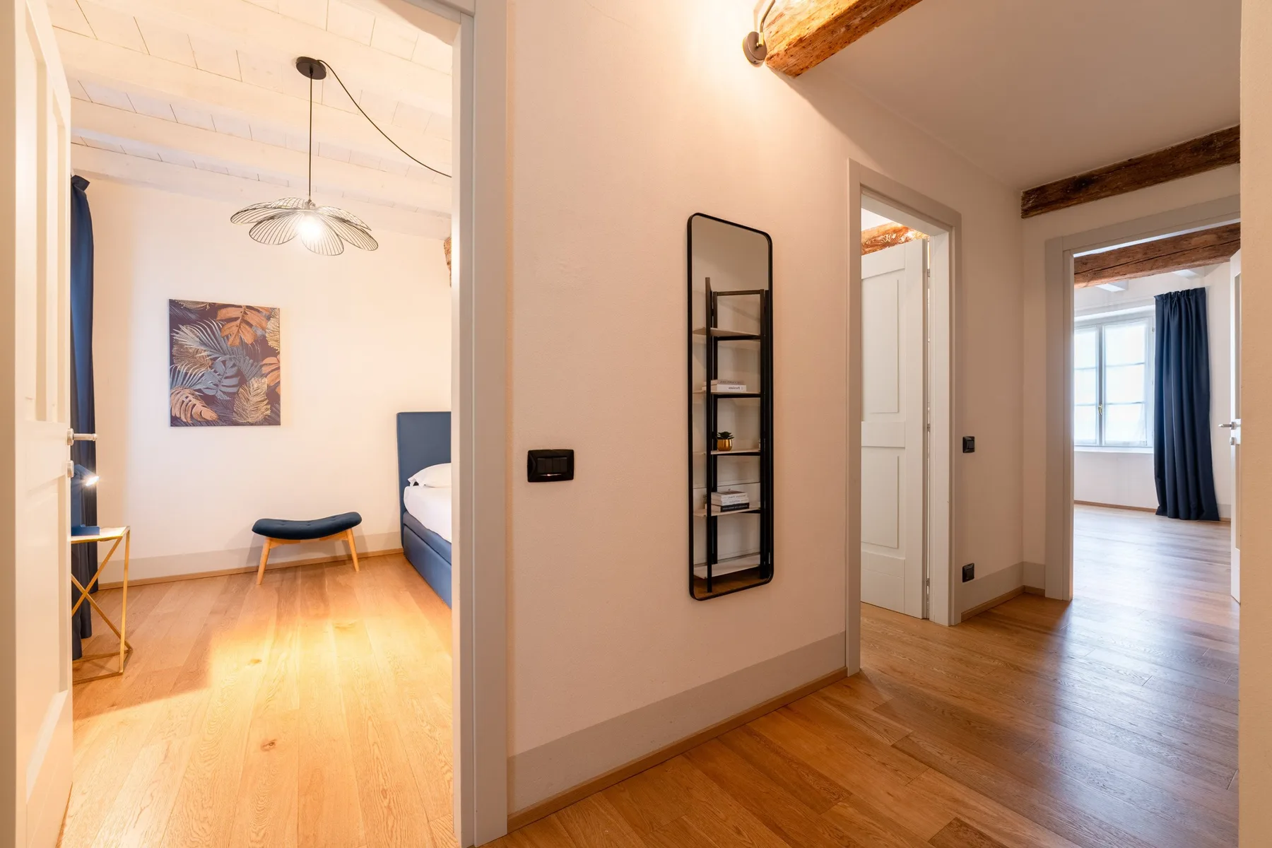 Un pasillo luminoso da a habitaciones contiguas con suelo de madera y una ventana.