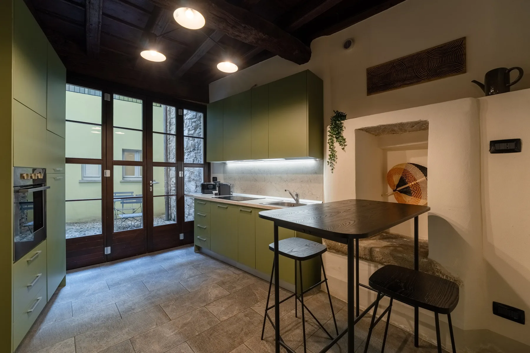Una cocina con muebles verdes, una isla central y puertas altas acristaladas.