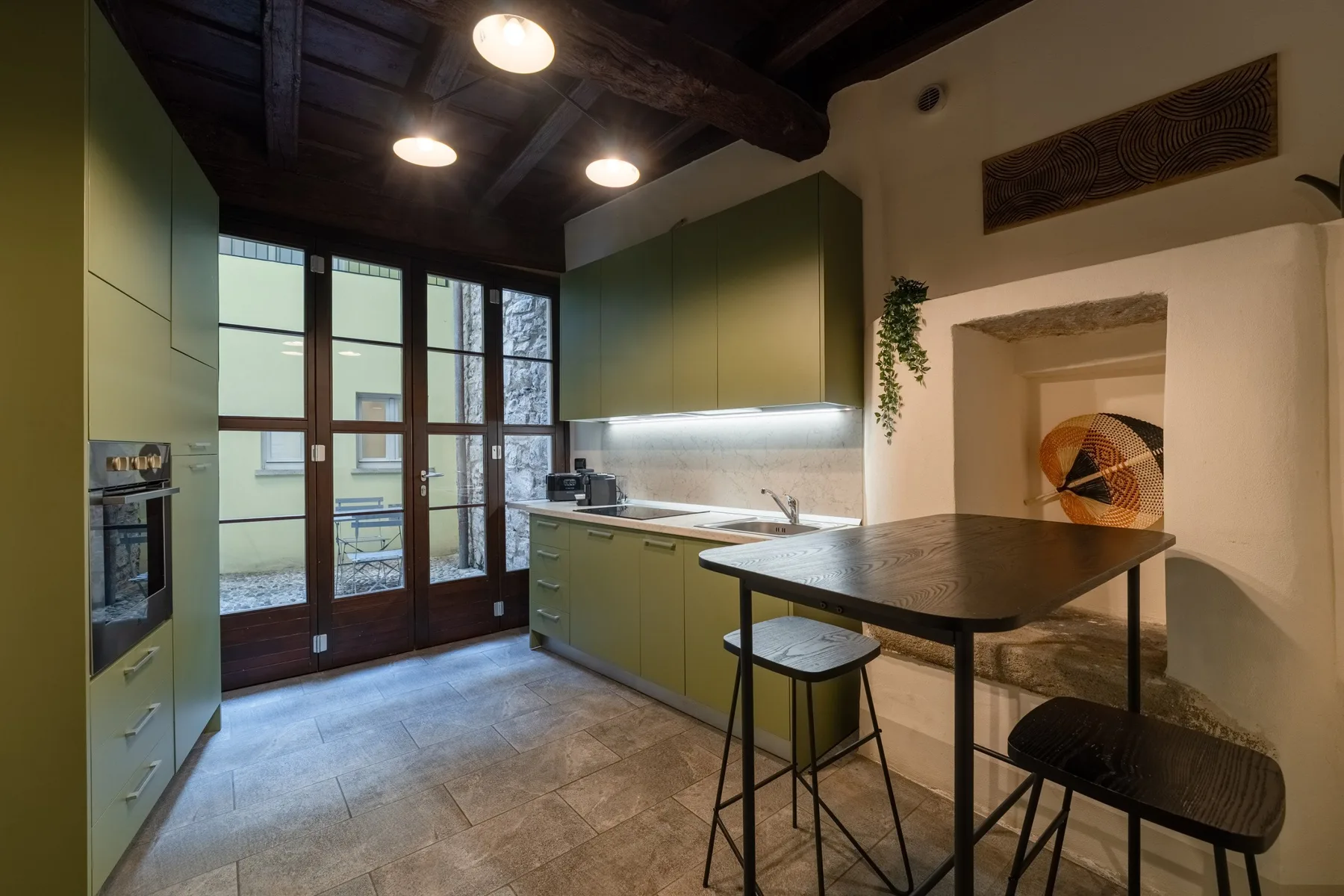 Una cocina con gabinetes verdes, una mesa de comedor y puertas de vidrio.
