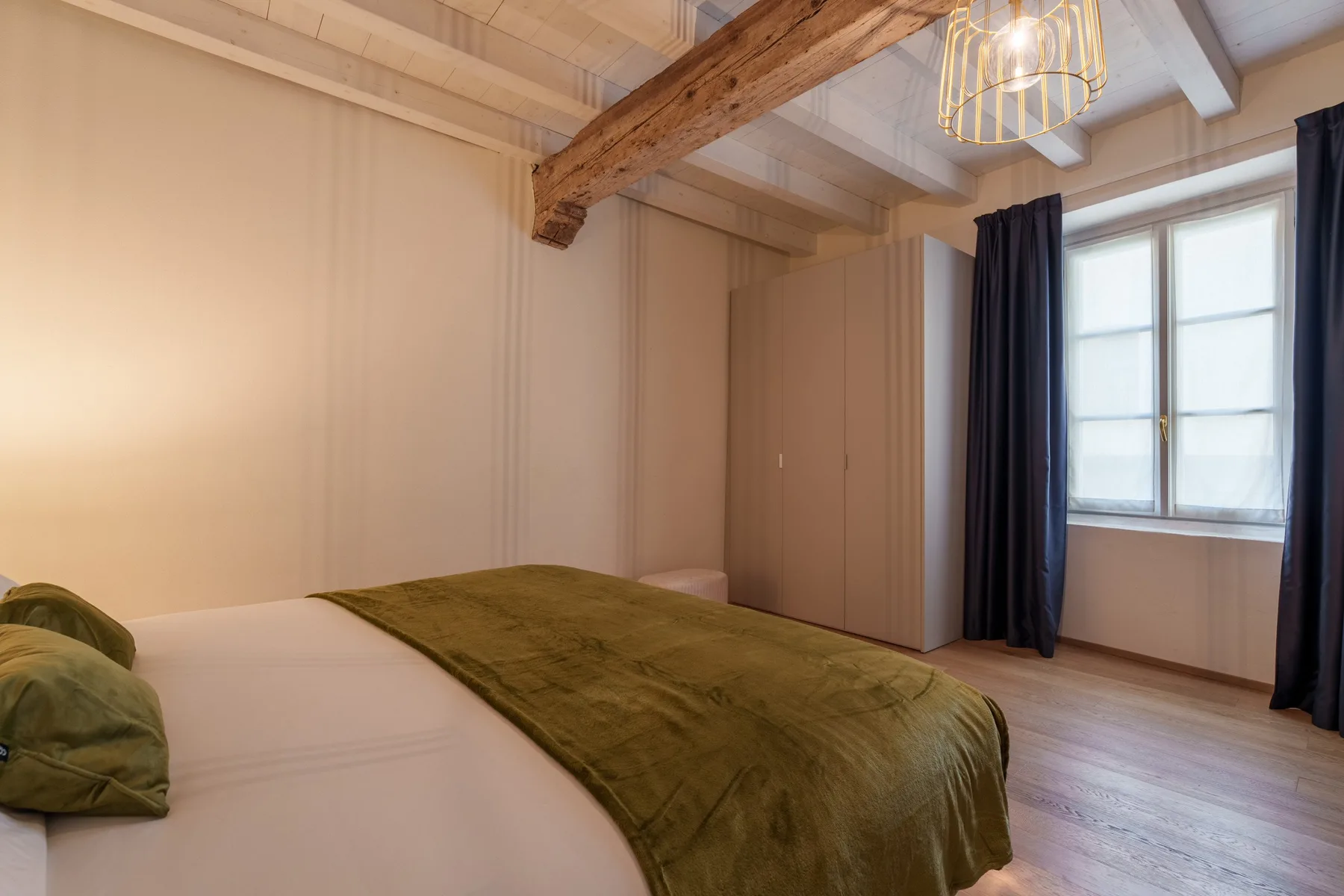 Un dormitorio con una cama, una colcha verde, un armario y una ventana.