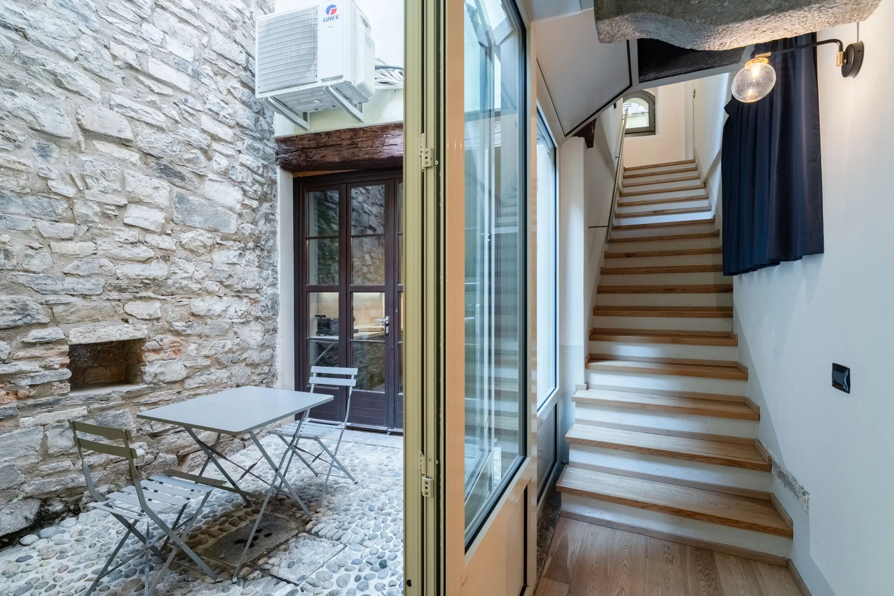 Un patio de piedra con una mesa pequeña junto a una escalera interior.