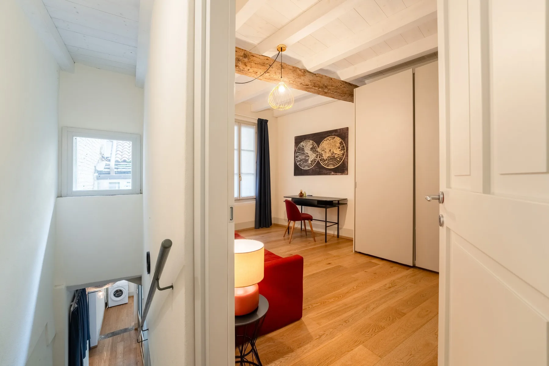 Se ve una habitación pequeña con un escritorio y asientos rojos a través de una puerta abierta.