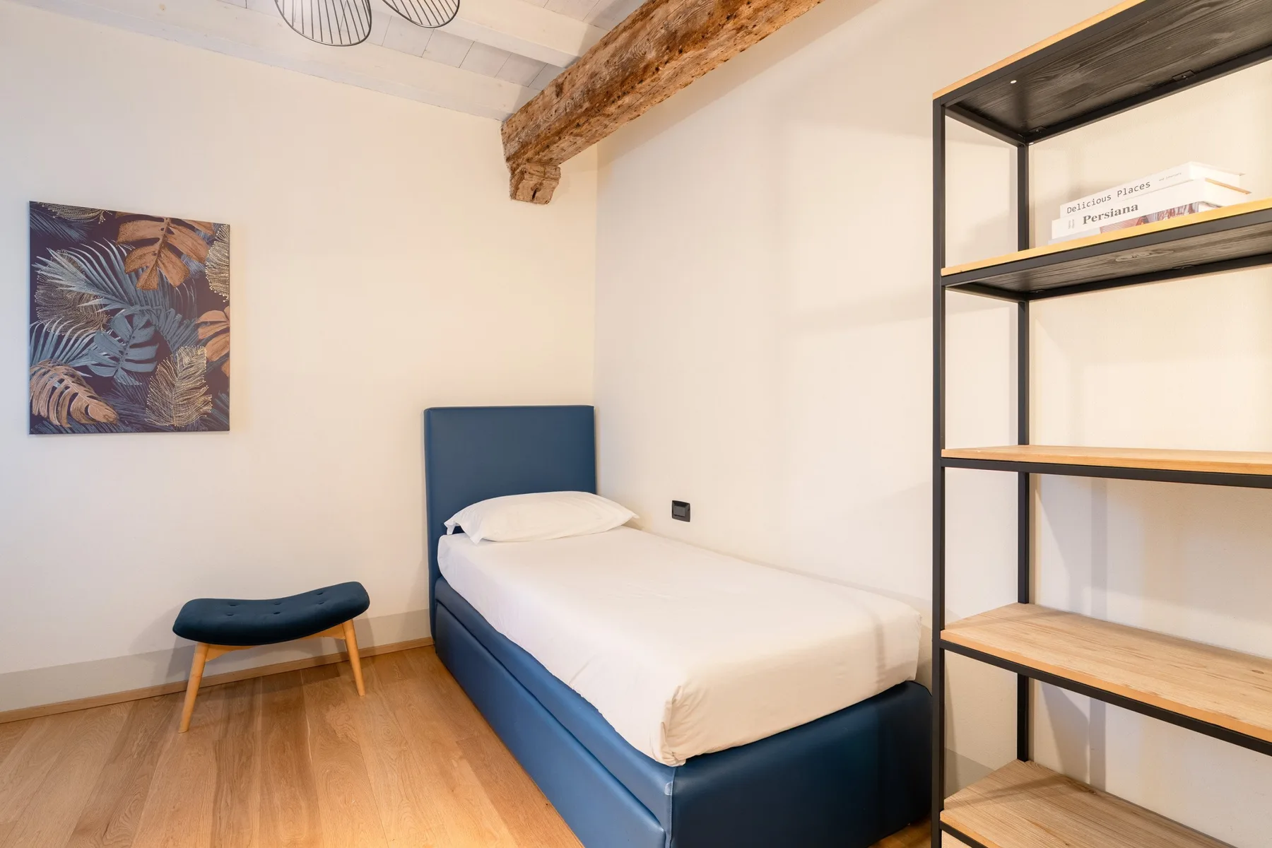 Un dormitorio con una cama individual, un pequeño taburete y estanterías abiertas.