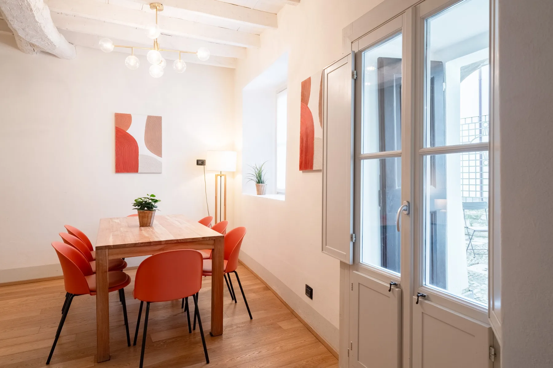 Un comedor luminoso con una mesa de madera, asientos rojos y grandes ventanas.