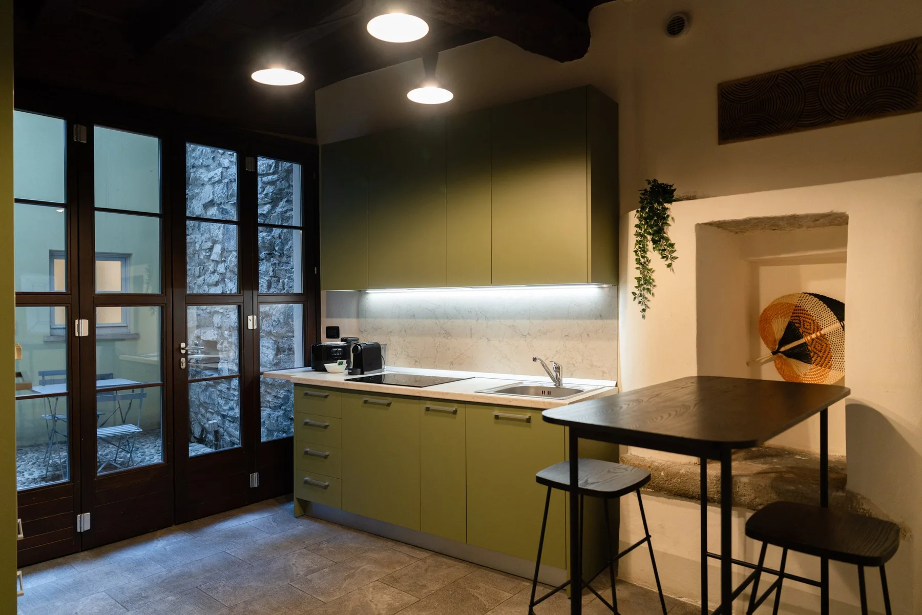 Una cocina moderna con armarios verdes, una encimera oscura y una pequeña mesa de comedor.