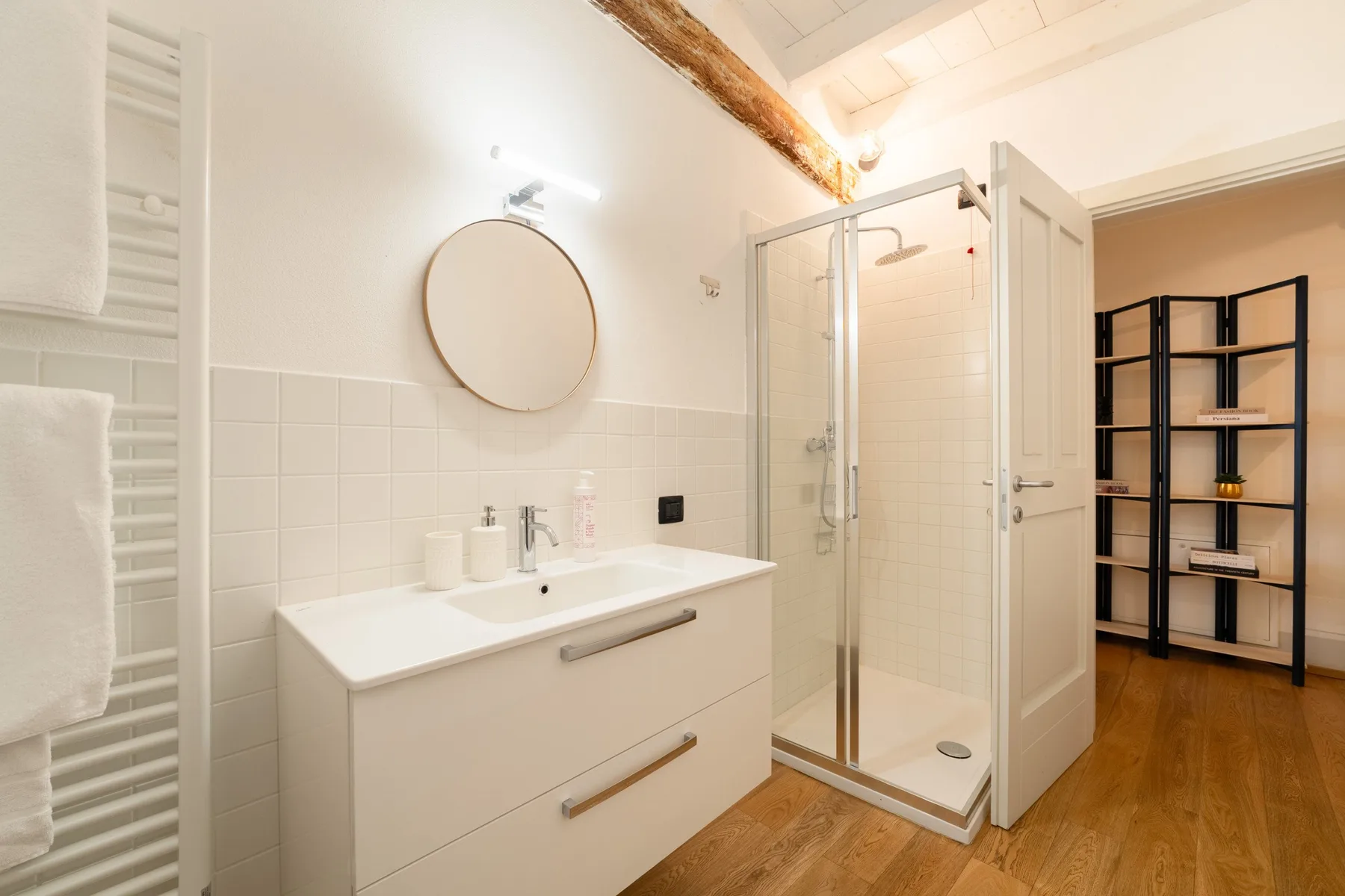 Un baño luminoso con lavabo, espejo redondo y ducha de cristal.
