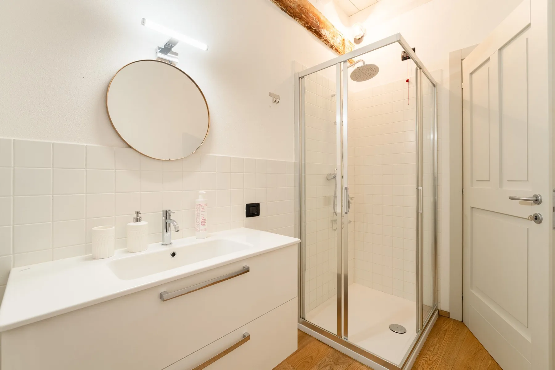 Un baño luminoso con lavabo, espejo redondo y ducha de cristal.