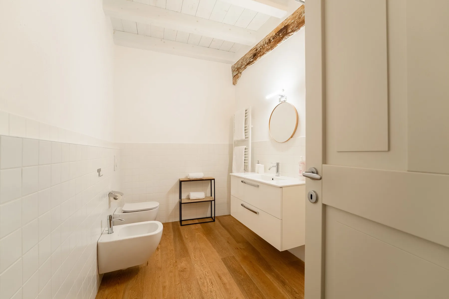 Un baño luminoso con bañera, lavabo y suelo de madera.