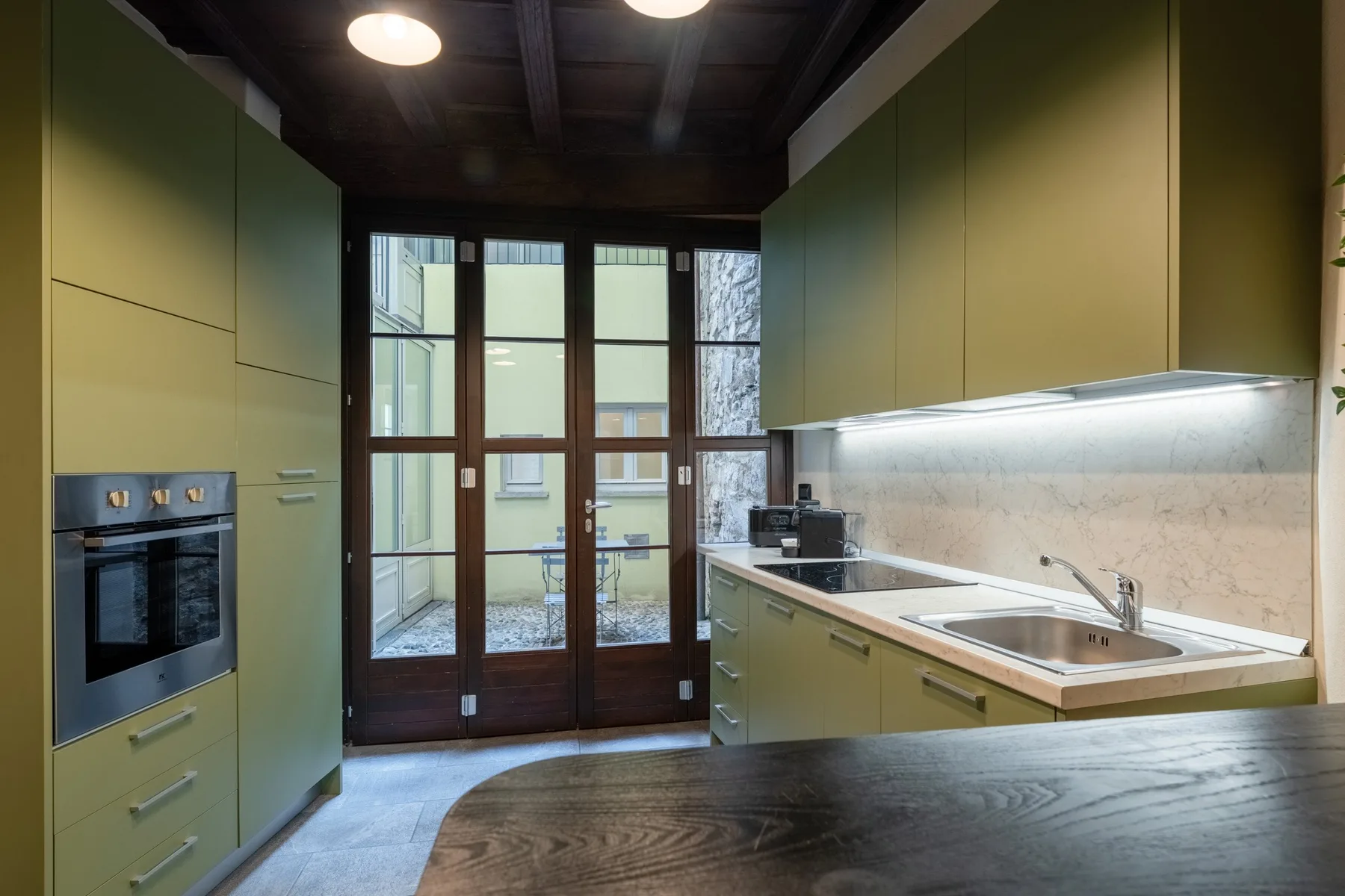 Una cocina moderna con gabinetes verdes, un fregadero y puertas de vidrio.