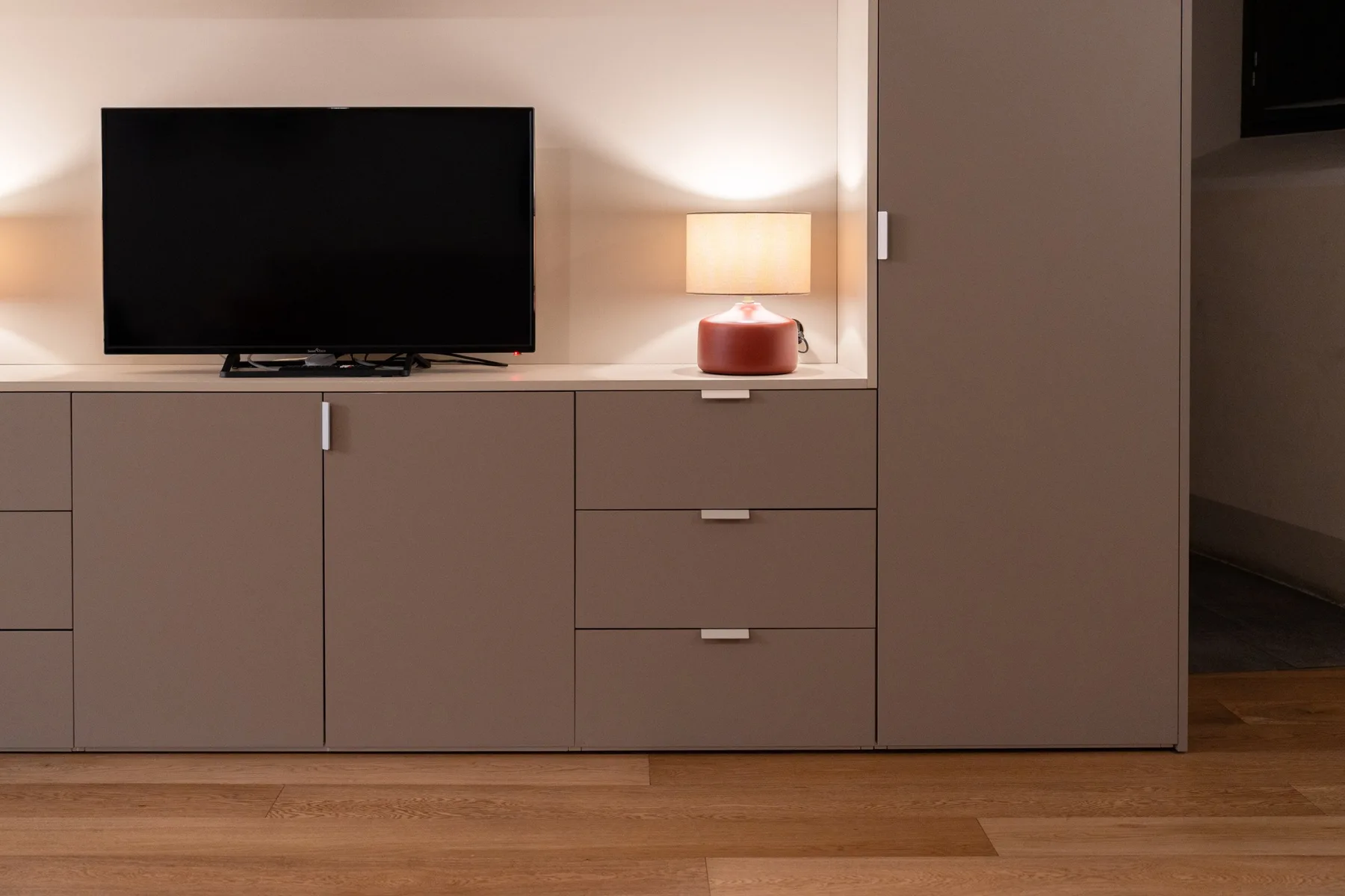 Un televisor y una lámpara de mesa están sobre un mueble empotrado en una habitación suavemente iluminada.