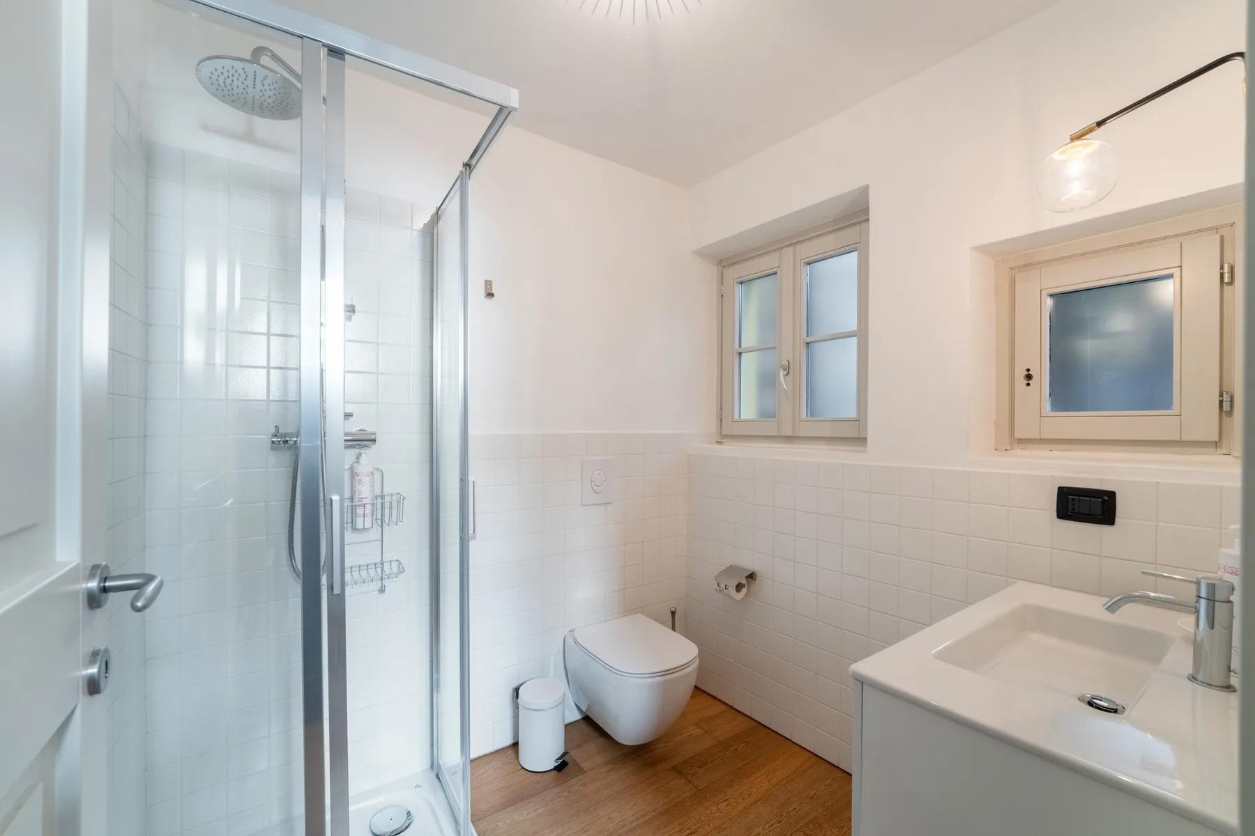 Un baño luminoso con ducha de vidrio, inodoro suspendido y lavabo con mueble.