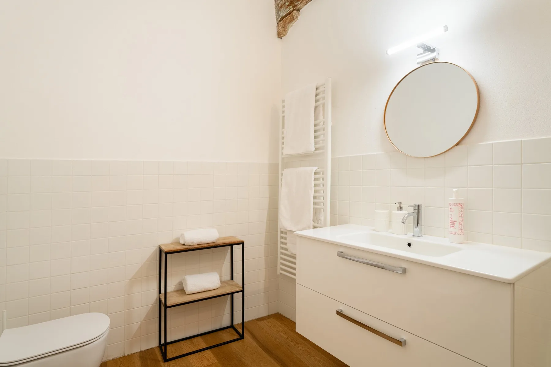 Un baño luminoso con lavabo, espejo redondo y toallero.