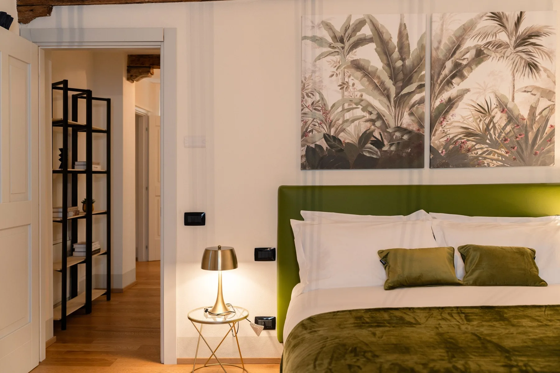 Un dormitorio con cabecero verde, almohadas blancas y arte botánico en la pared.
