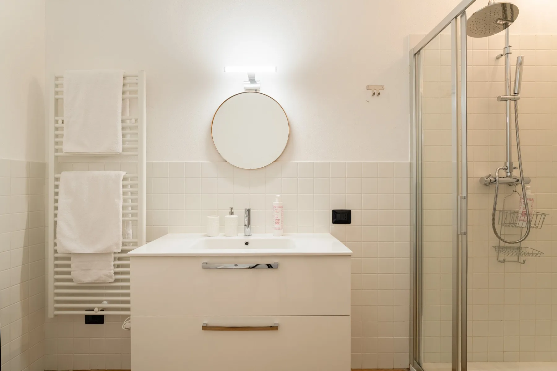 Un baño luminoso con tocador, espejo redondo y ducha de vidrio.