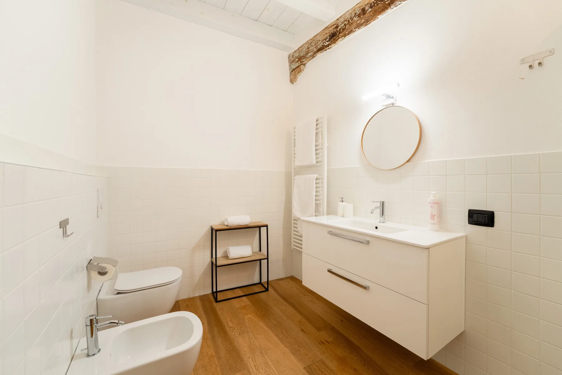 Un baño luminoso con lavabo, espejo redondo, inodoro y bidé.