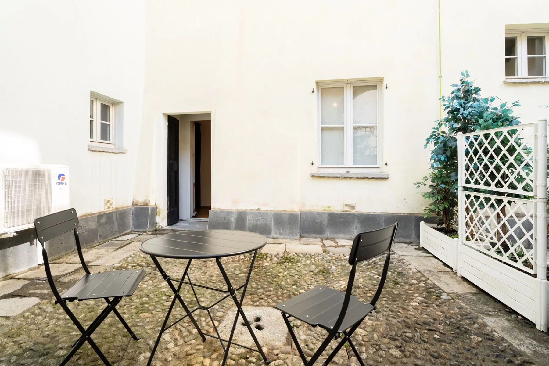 Un patio exterior con una mesa pequeña y asientos junto a un edificio de color claro.