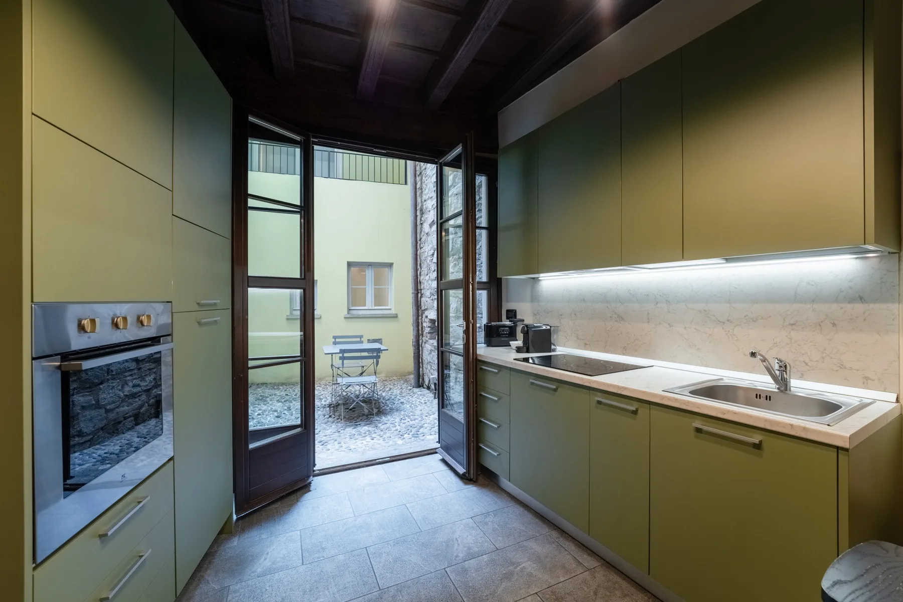 Una cocina moderna con gabinetes verdes y puertas de vidrio que dan a un pequeño patio.