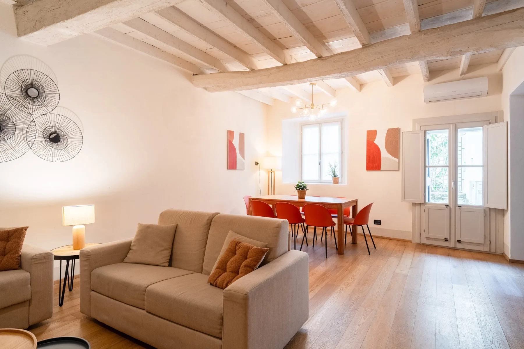 Una luminosa sala de estar y comedor con asientos, una mesa de comedor y vigas expuestas.