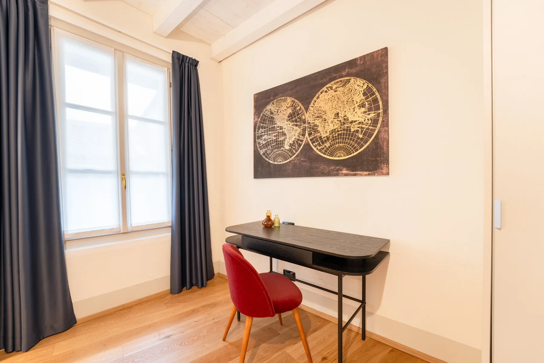 Una habitación luminosa con escritorio, asiento rojo y arte enmarcado.