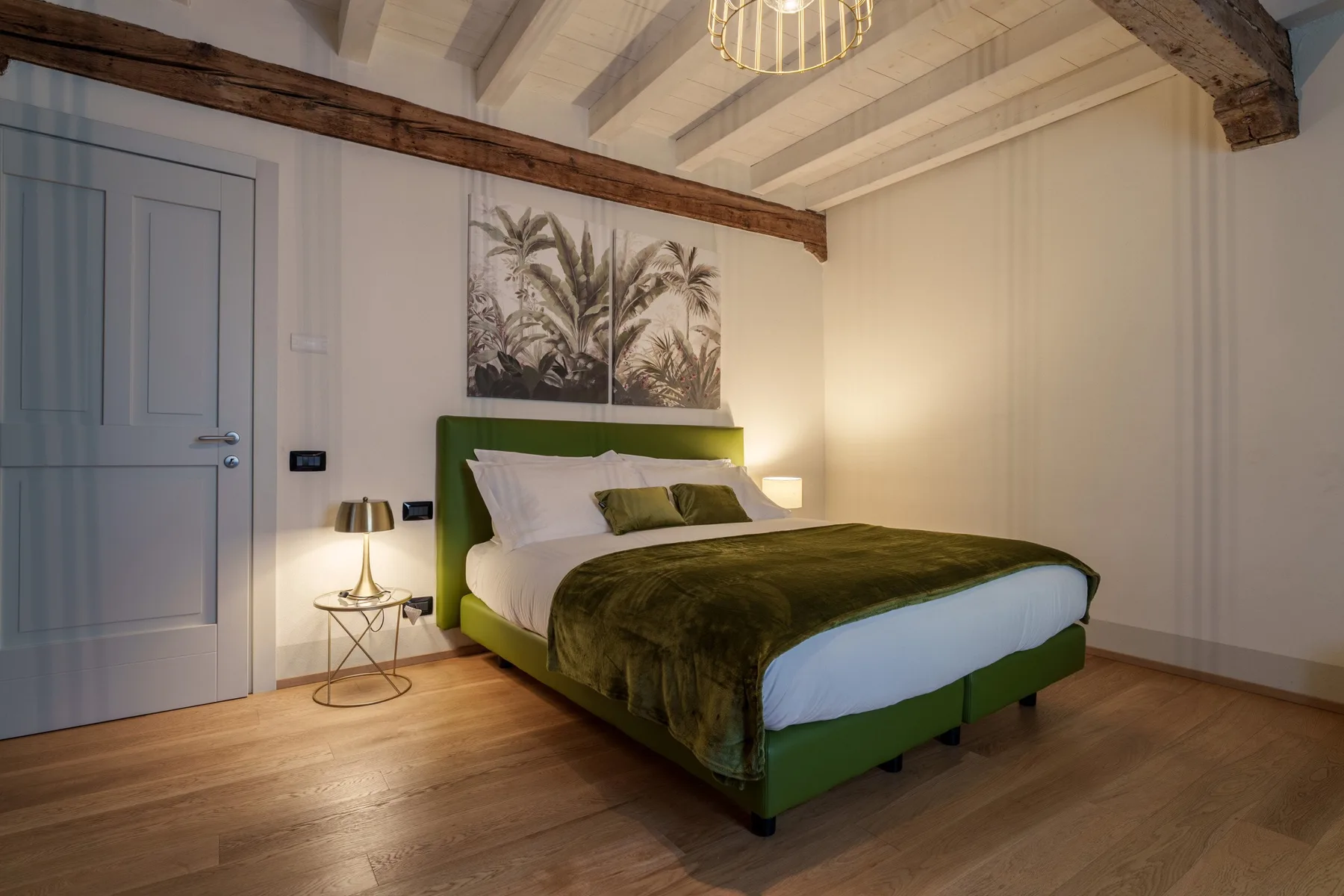 Un dormitorio con una cama verde bajo una lámina de palmeras.