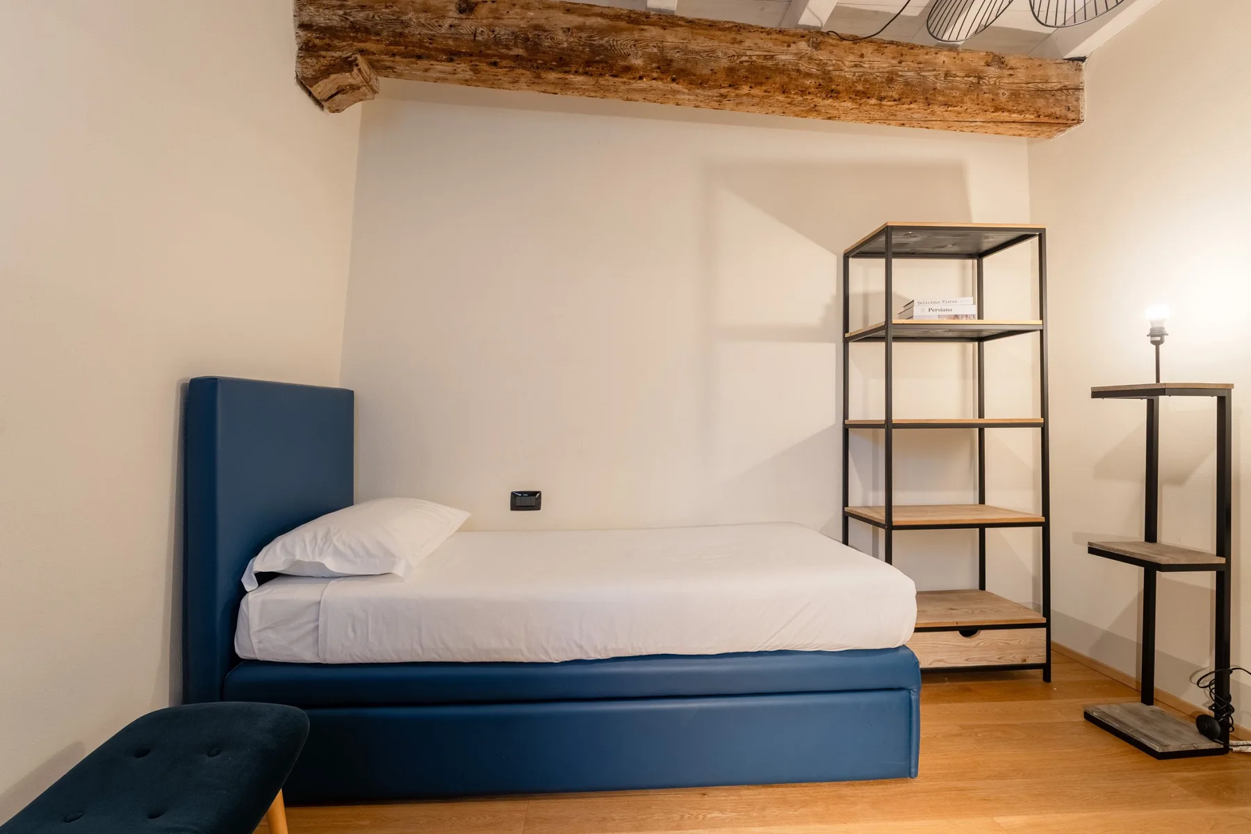 Un dormitorio con una cama azul, ropa de cama blanca y estanterías abiertas.
