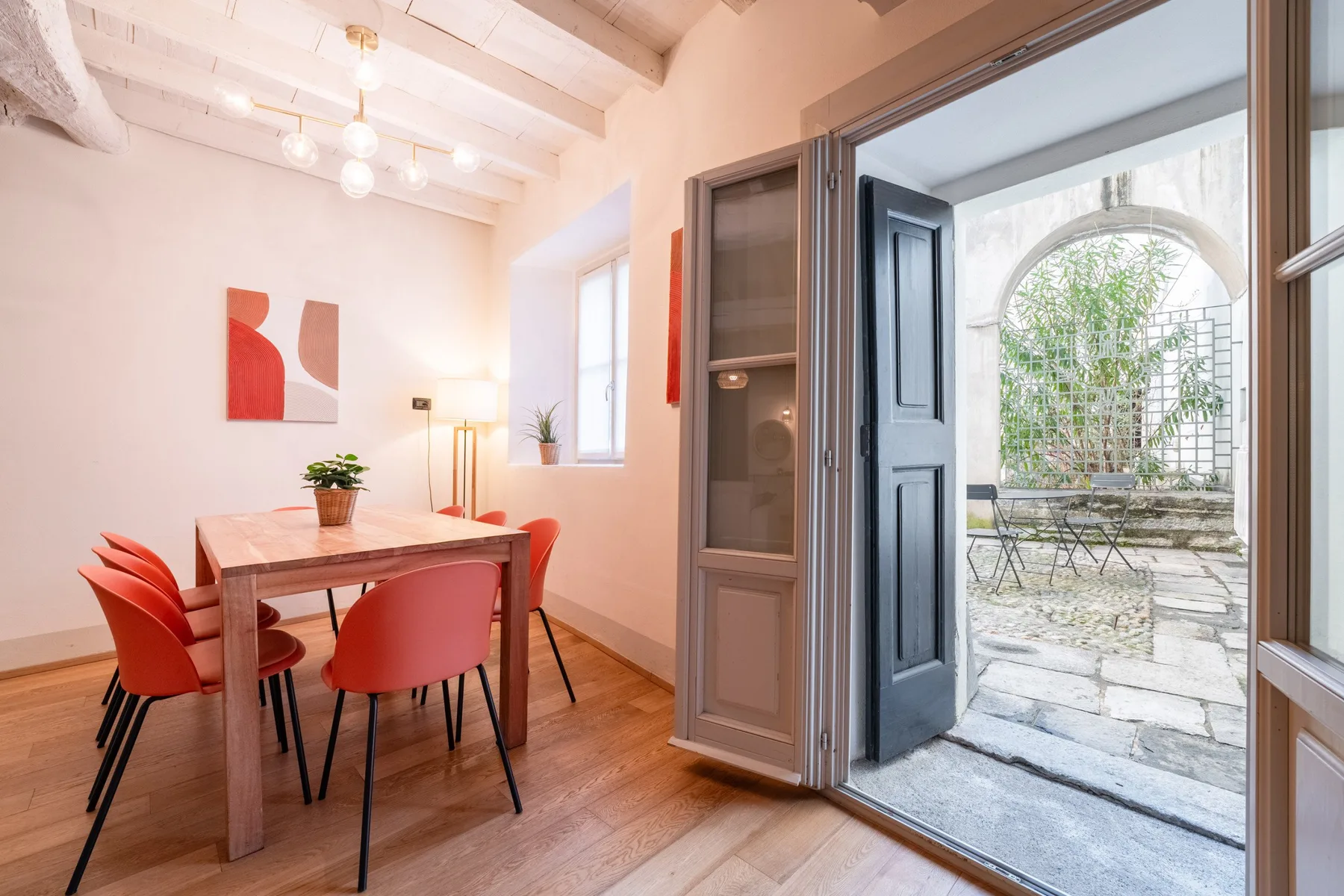 Un comedor con mesa de madera y asientos rojos da a un patio de piedra.