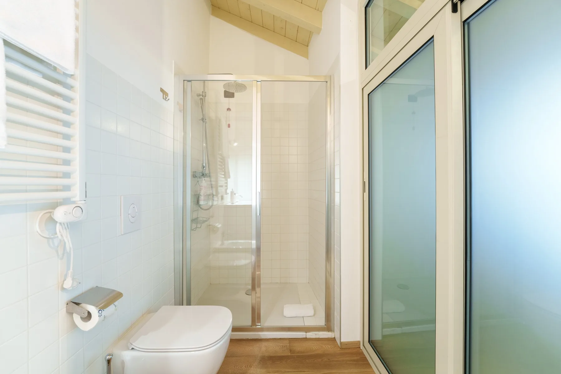 Un baño luminoso con azulejos, ducha de vidrio e inodoro.