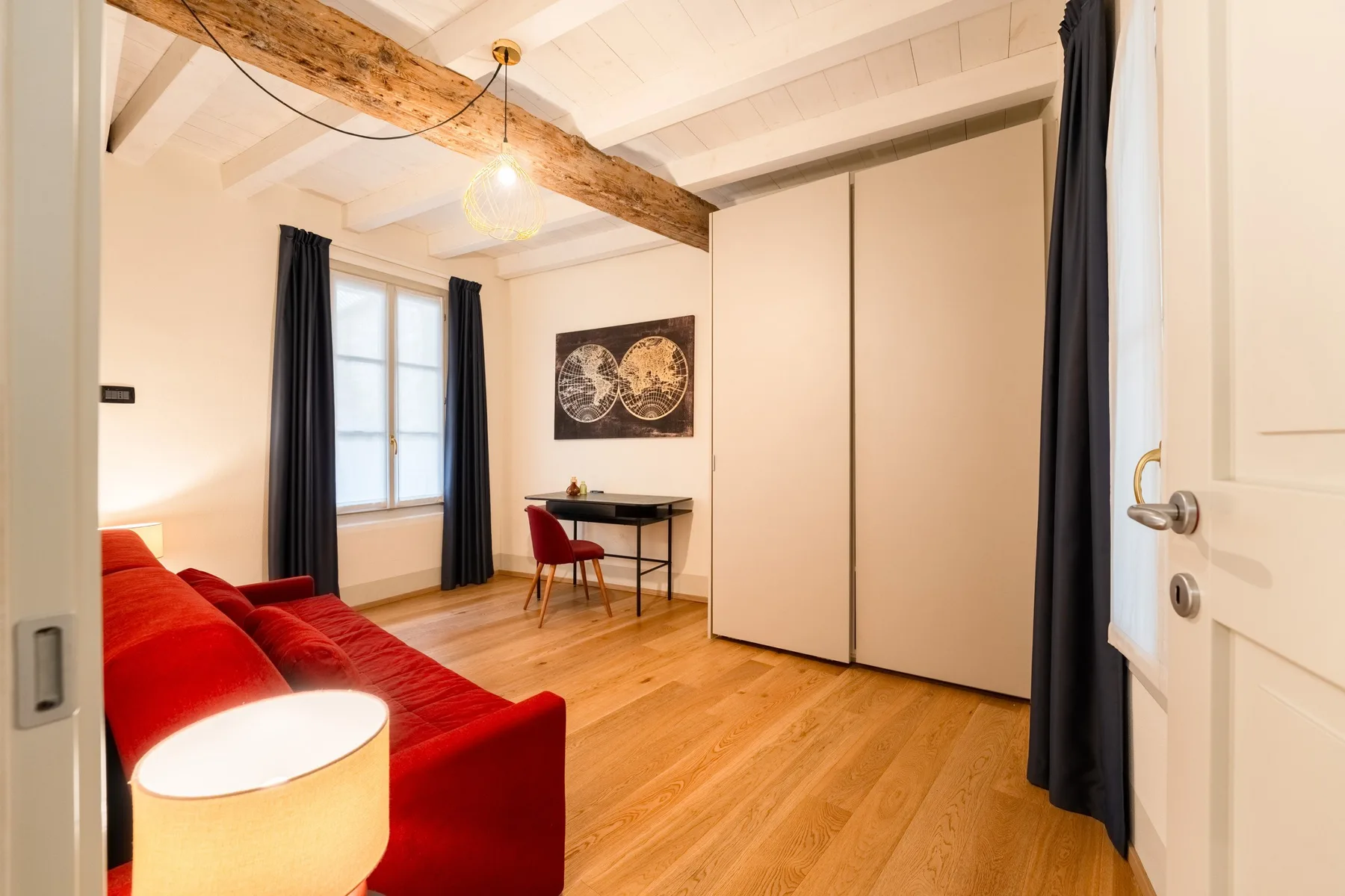 Una luminosa sala de estar con asientos rojos, un escritorio pequeño y suelo de madera clara.
