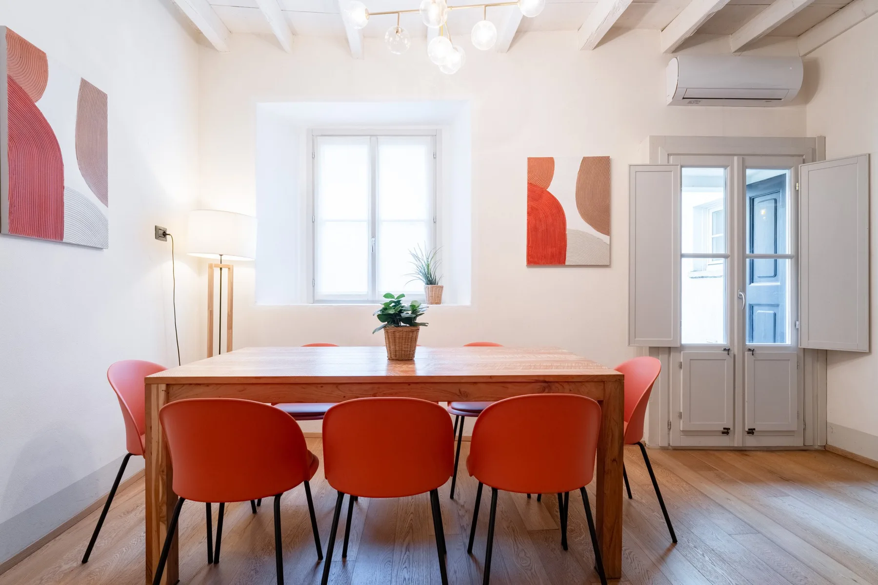 Un comedor luminoso con una mesa de madera, asientos rojos y arte abstracto en las paredes.