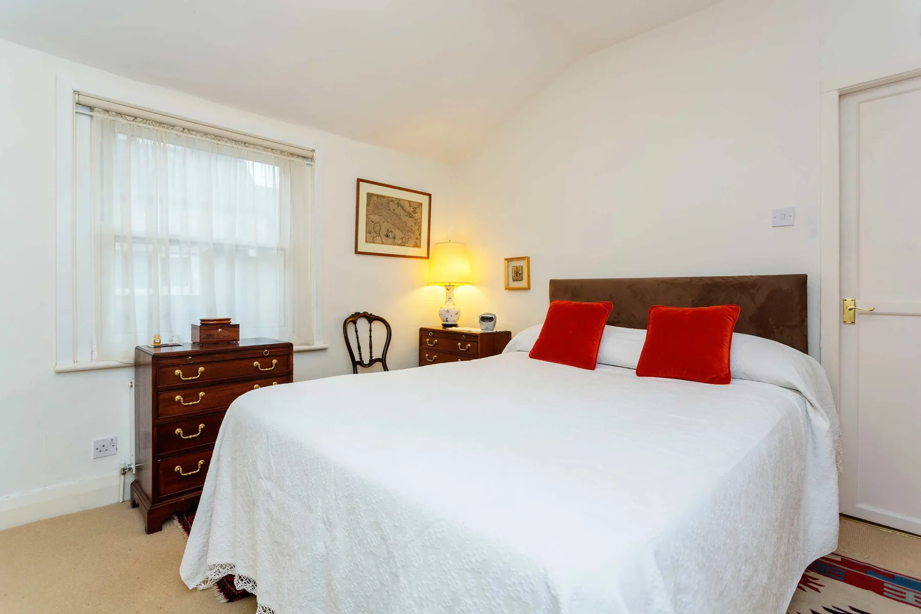 Un dormitorio con una cama blanca, almohadas rojas y una ventana.