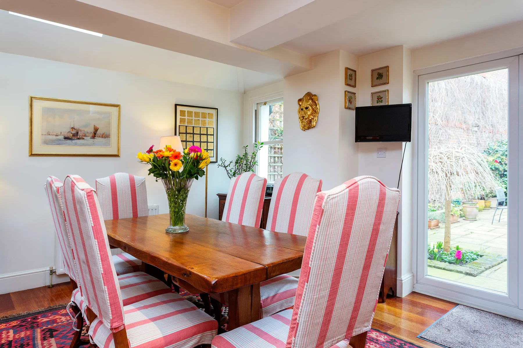 Comedor con mesa de madera, asientos a rayas y flores.