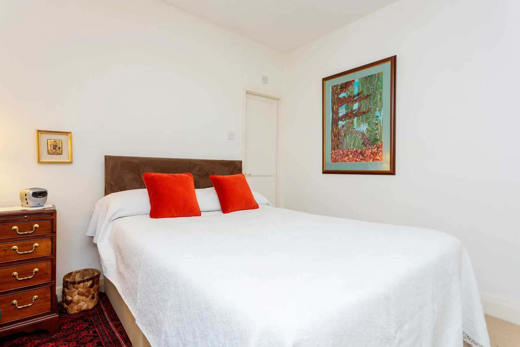 Un dormitorio luminoso con ropa de cama blanca y cojines rojos.