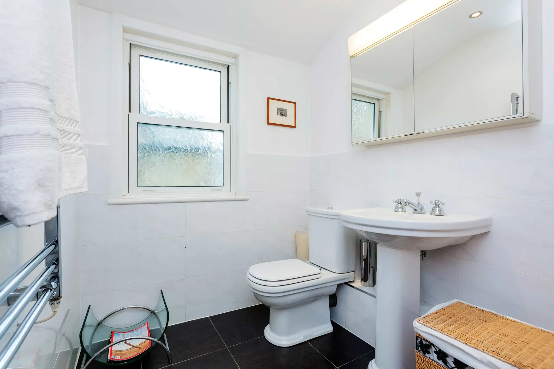 Un baño luminoso con una ventana, un inodoro y un lavabo con pedestal.