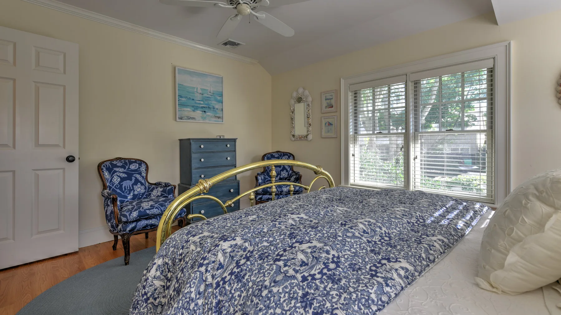 Un dormitorio con una cama cubierta con ropa de cama floral azul y blanca junto a grandes ventanas.