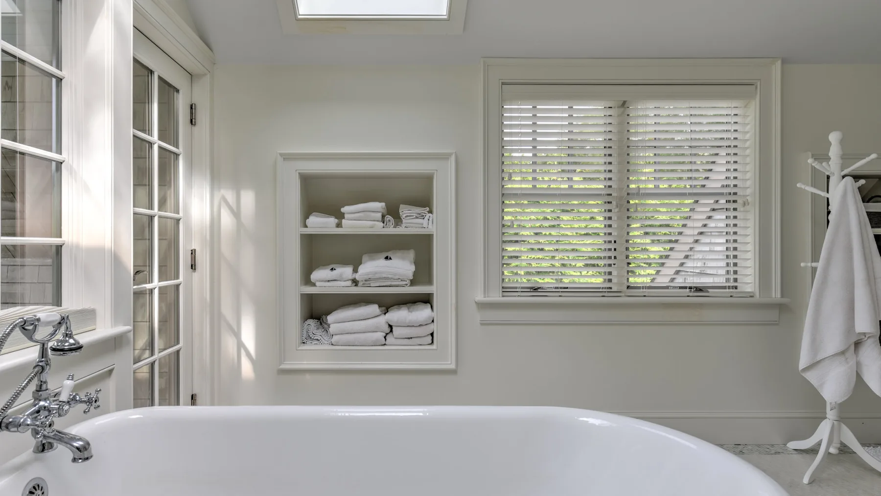Un baño luminoso con bañera y una ventana con persianas.