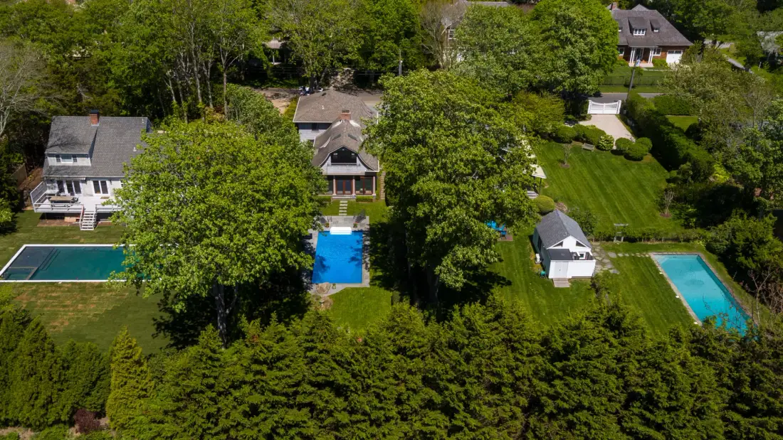 Vista aérea de casas y jardines entre árboles, con varias piscinas al aire libre.