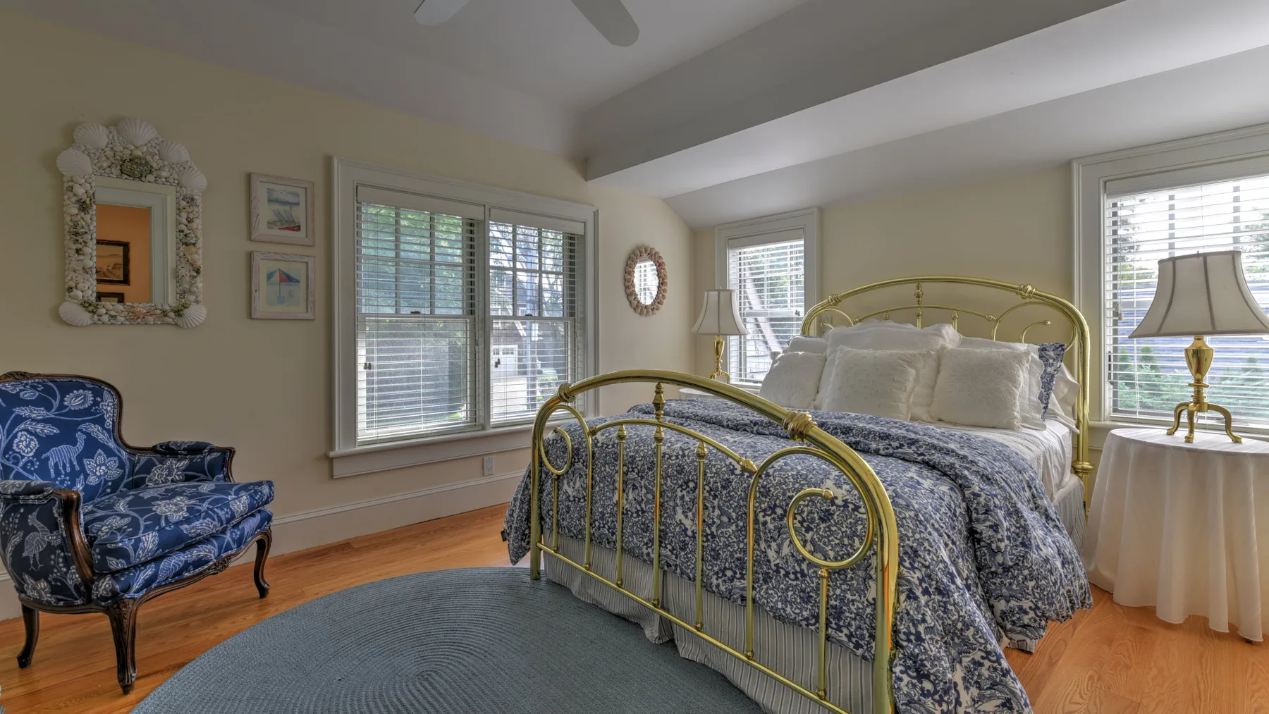 Un dormitorio con una cama de latón y un sillón estampado junto a las ventanas.