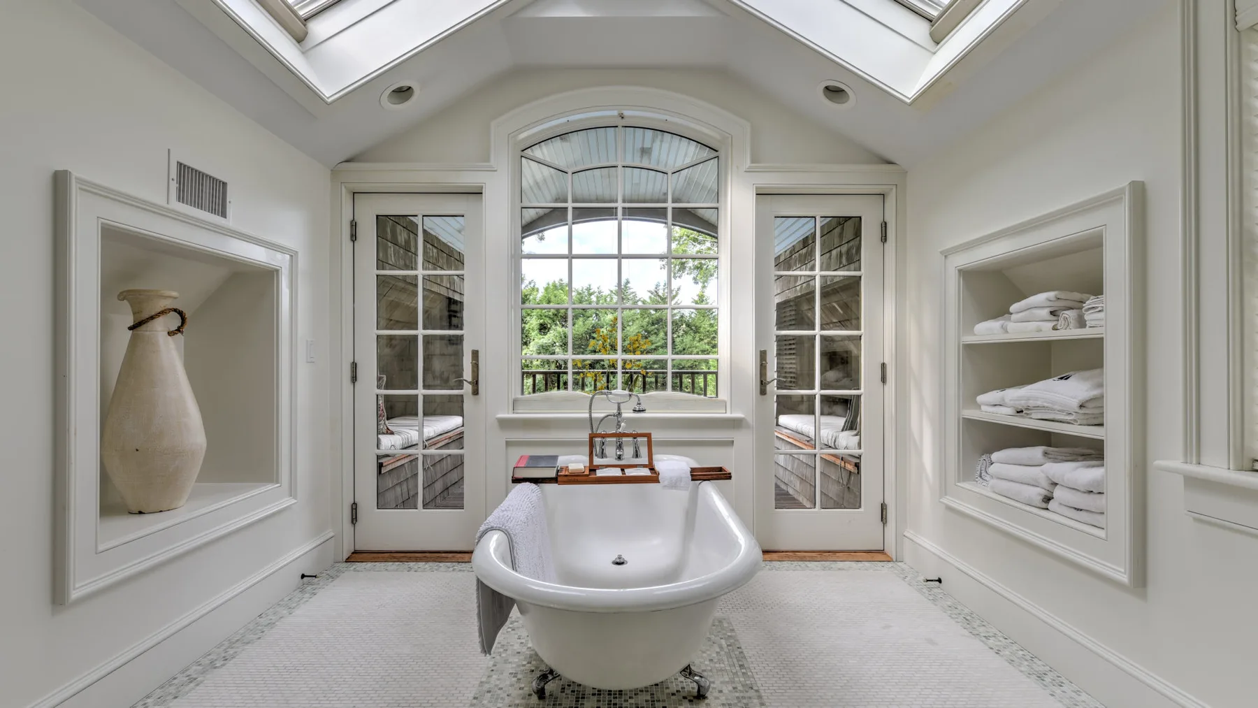 Un baño luminoso con una bañera exenta bajo una gran ventana arqueada.