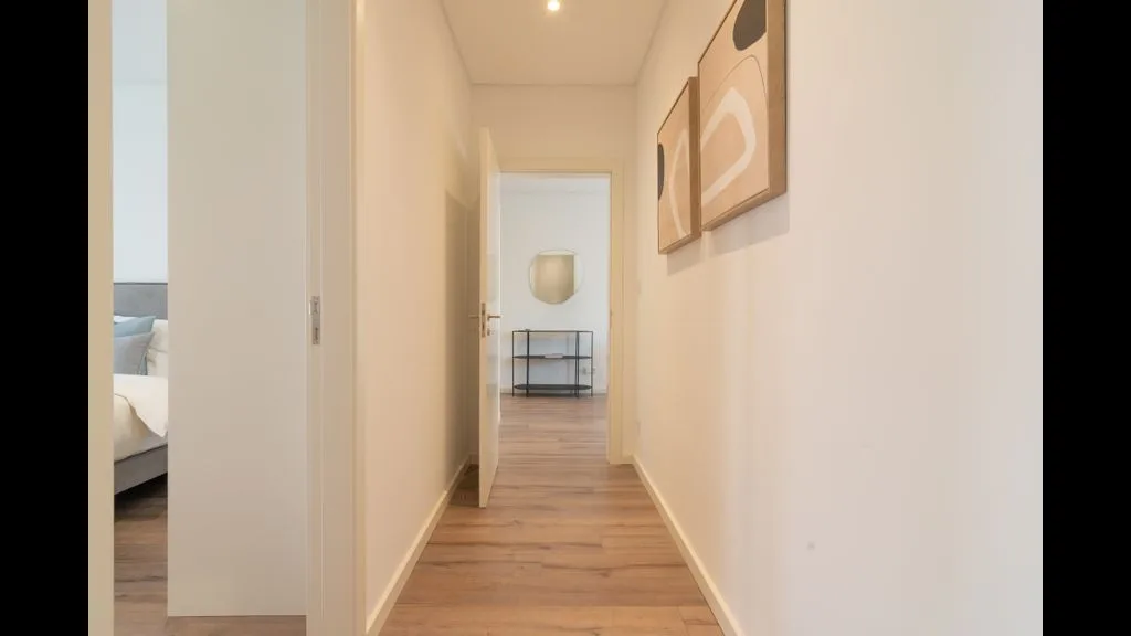 Un pasillo luminoso con suelo de madera clara y cuadros en la pared.