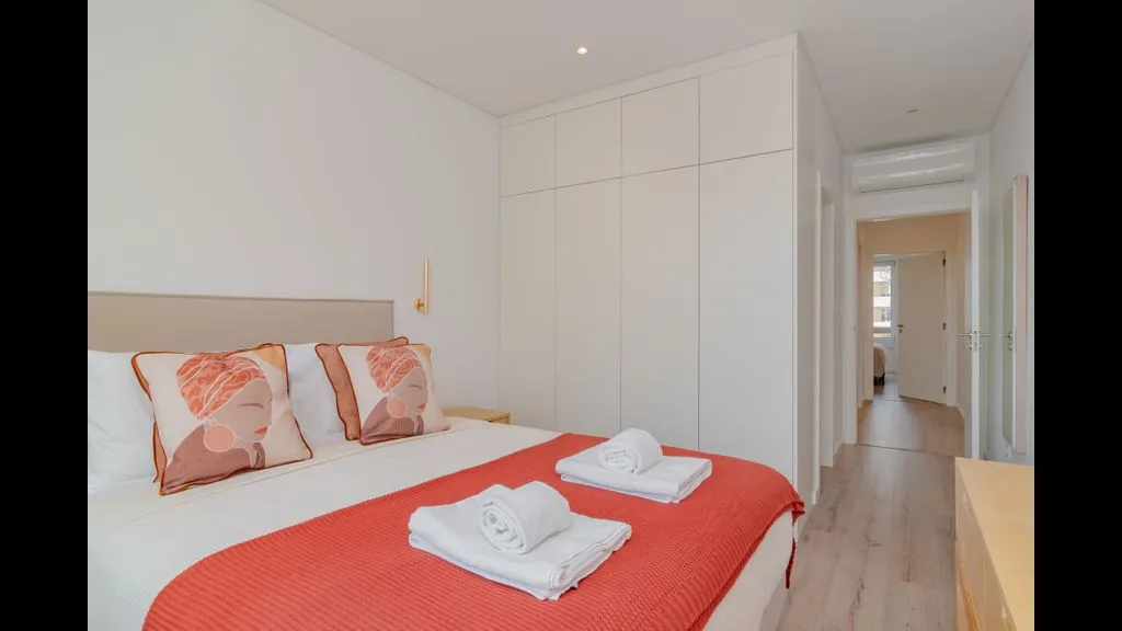 Un dormitorio con una cama cubierta por una manta coral y toallas dobladas.