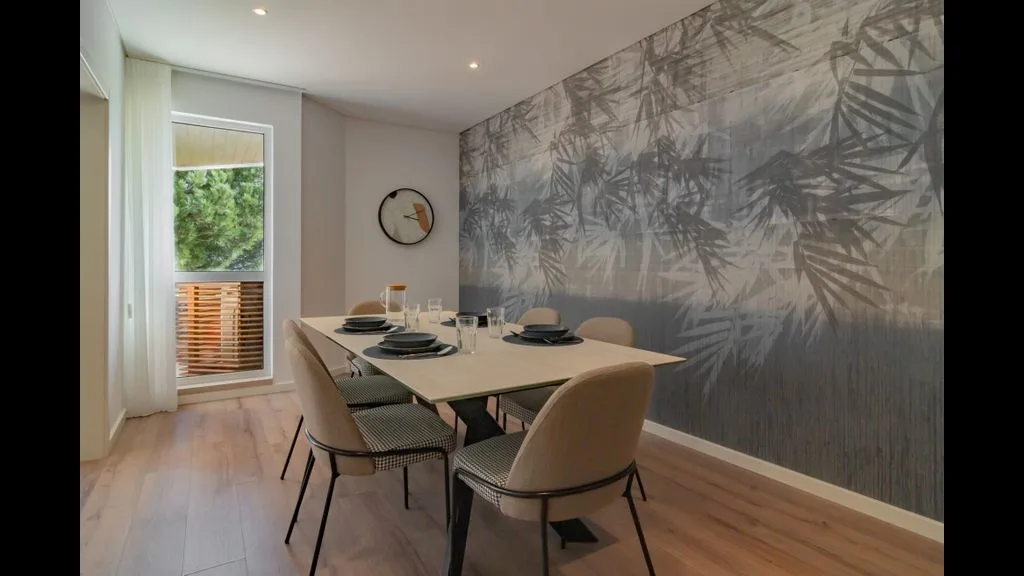 Comedor con una mesa y sillas junto a una pared decorativa con motivos de hojas.