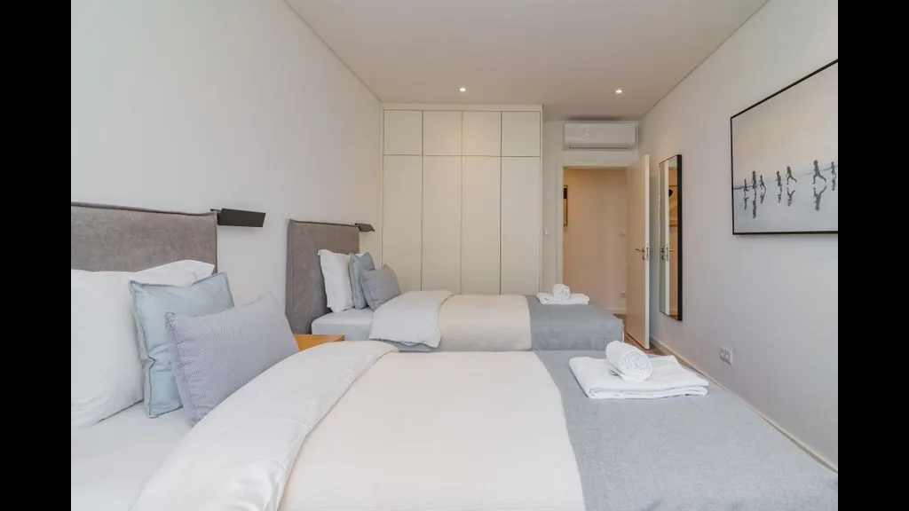 Dormitorio luminoso con dos camas, ropa de cama clara y armarios empotrados.
