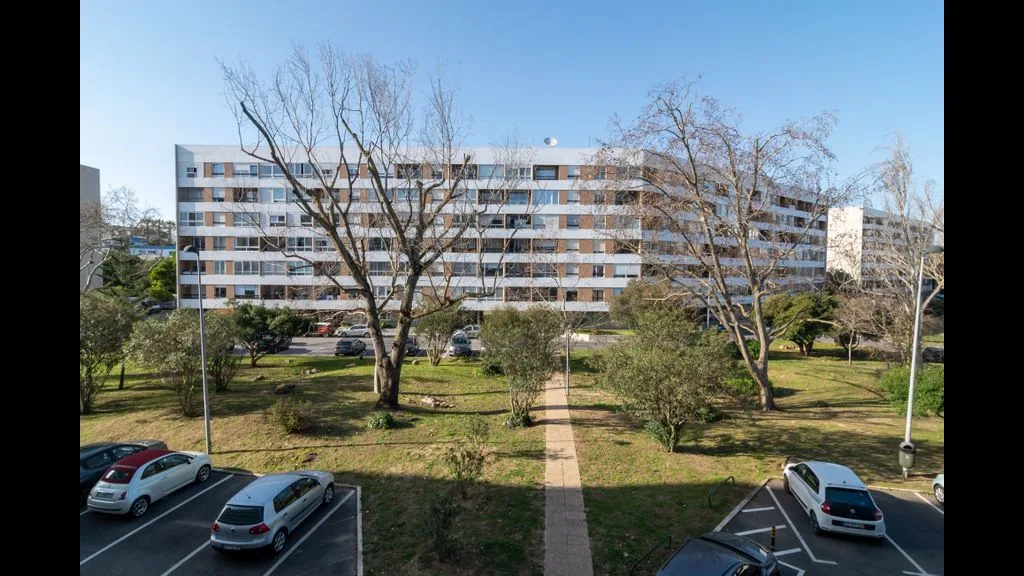 Vista de un edificio residencial tras una zona verde y un área de estacionamiento.