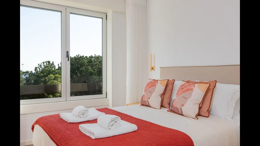 Un dormitorio con una colcha roja, cojines estampados y una ventana grande.