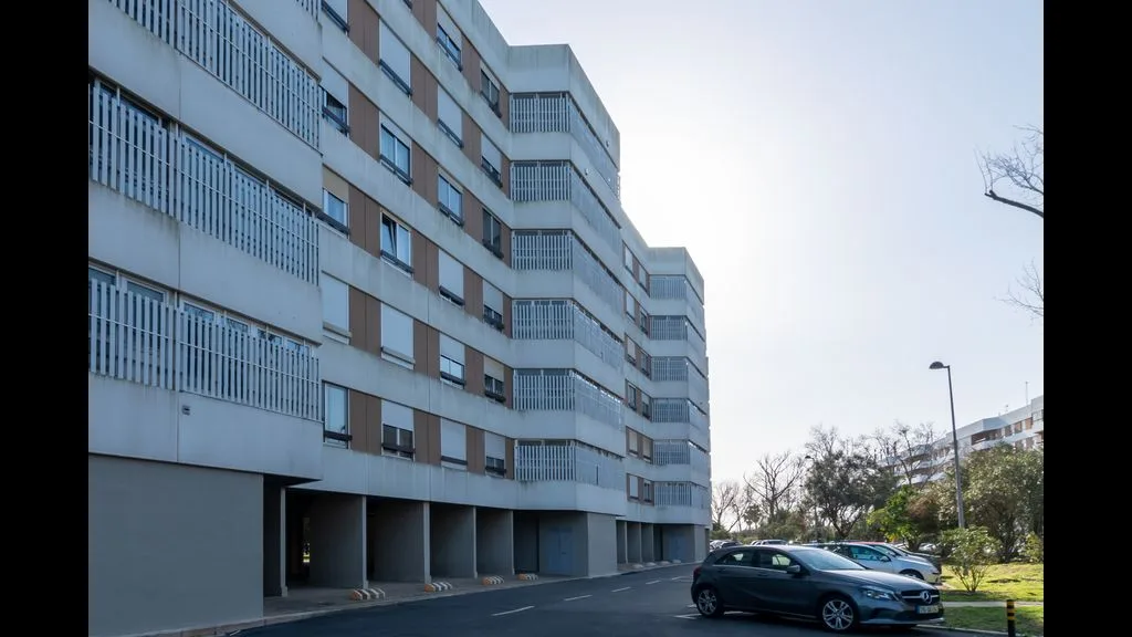 Un edificio de apartamentos de varias plantas con balcones junto a una calle pavimentada.