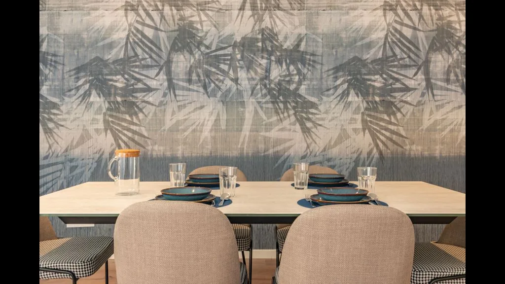 Un comedor con la mesa puesta y un mural de hojas en la pared.