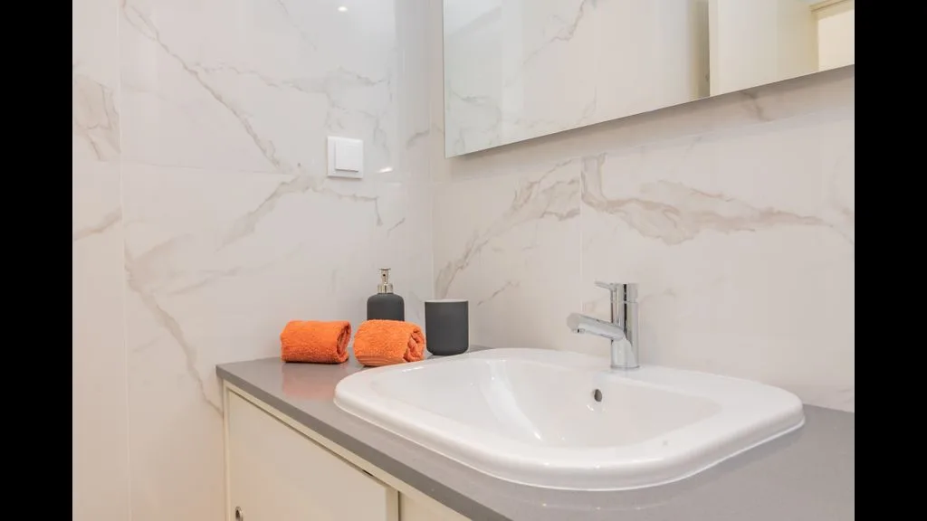 Un lavabo de baño con fregadero blanco, grifo y toallas dobladas.